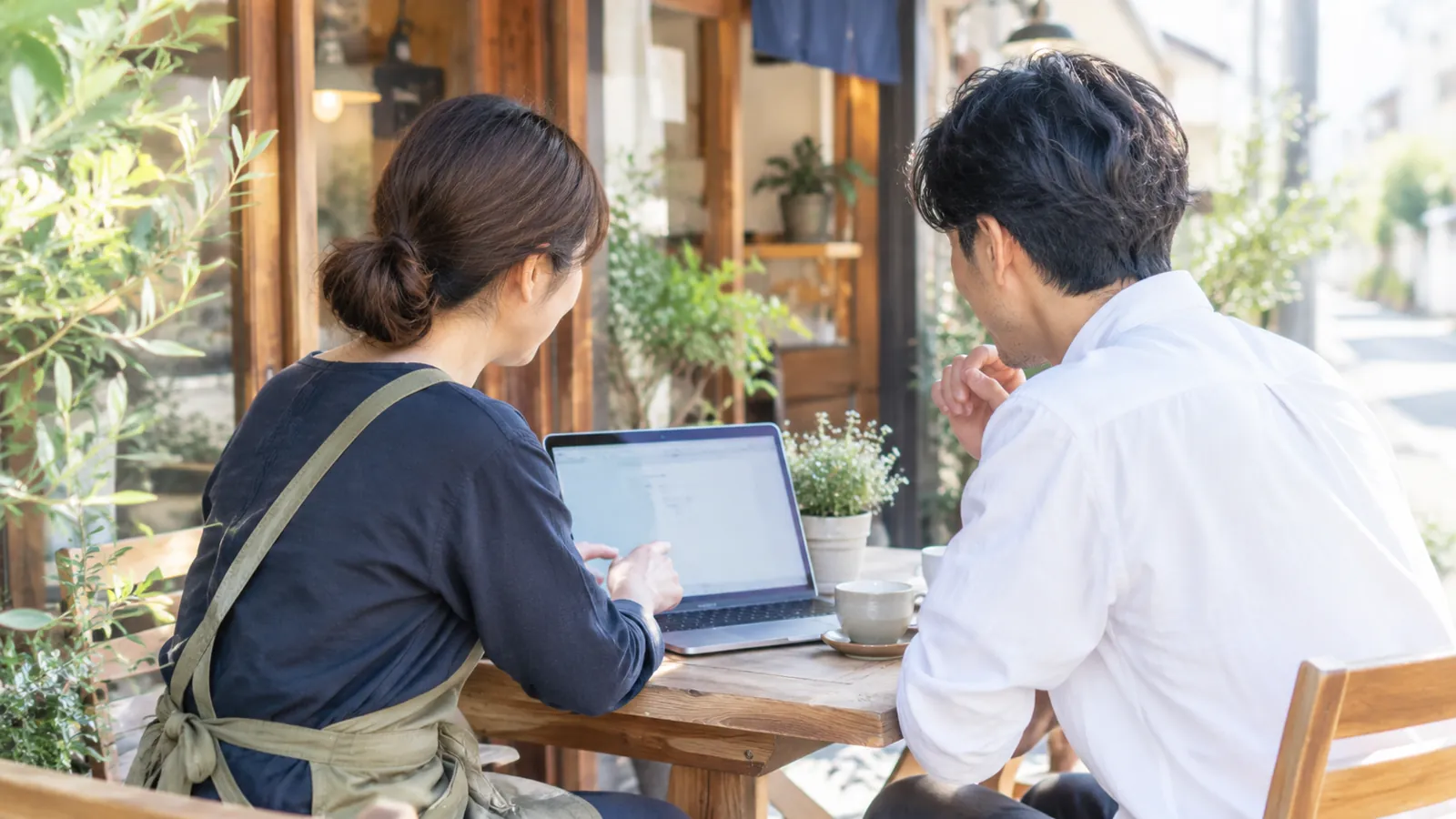さいたま市の小さなお店の店先で、店主がノートパソコンを見ながらホームページの相談をしている様子